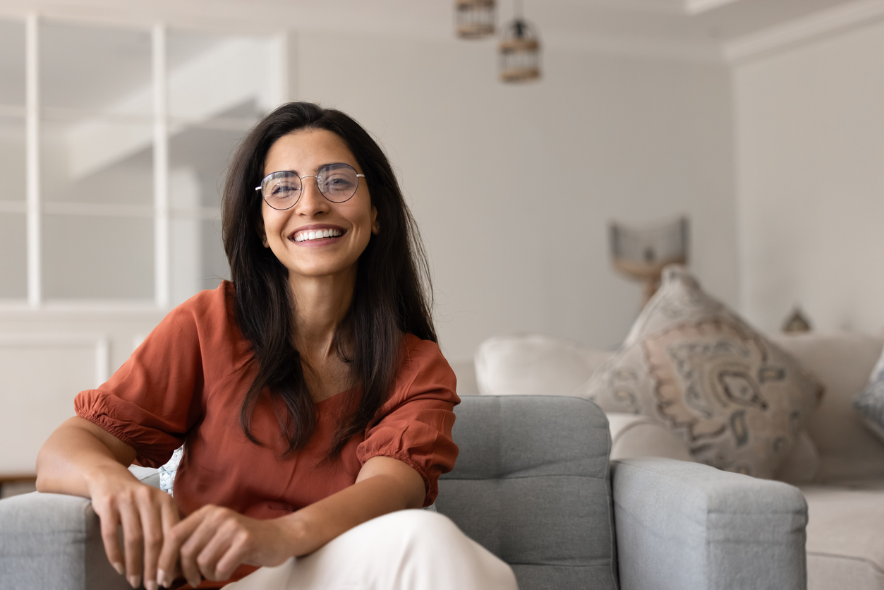 Cheerful young Hispanic woman in elegant eyeglasses sitting in armchair